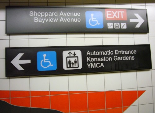 One sign of two has arrow and two pictos and reads Automatic Entrance Kenaston Gardens YMCA