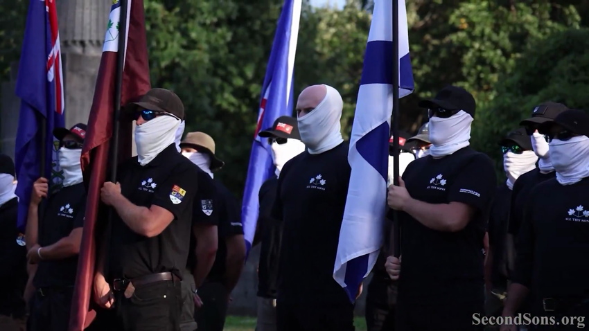 Overly serious men in identical branded polo shirts and white face coverings, some holding flagstaffs